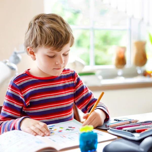 Niño de escuela feliz trabajador haciendo tarea durante el tiempo de cuarentena de la enfermedad pandémica de corona. Niño sano escribiendo con bolígrafo, quedándose en casa. Concepto de educación en el hogar —  Fotos de Stock