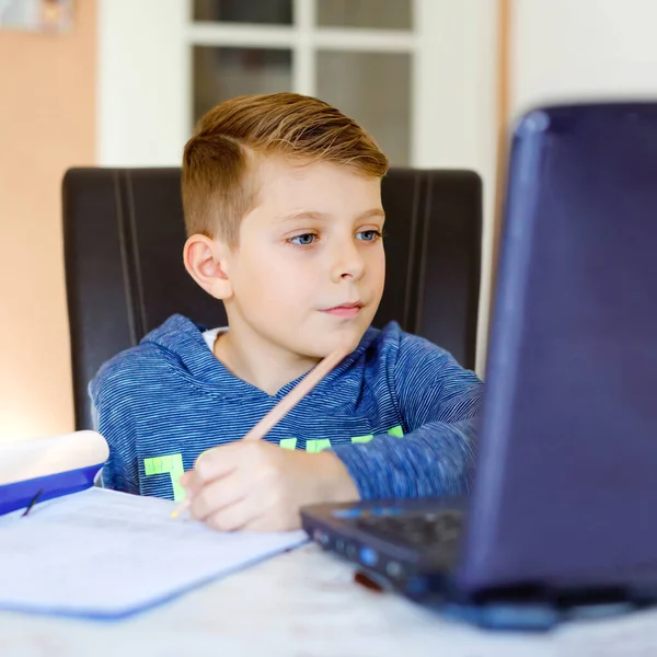 En liten skolpojke som gör läxor på datorn. Barn lär sig på datorn. Hårt arbetande pojke gör motion under karantänstid från koronapandemisk sjukdom. Hemskolekoncept. — Stockfoto