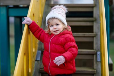 Küçük tatlı kız oyun alanında eğleniyor. Mutlu küçük çocuk tırmanışı, farklı ekipmanların üzerinde sallanmak ve kaymak. Renkli giysiler içinde soğuk bir günde. Çocuklar için aktif açık hava oyunu