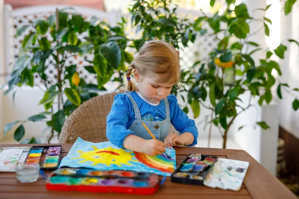 Pequena menina pintando arco-íris e sol com cores de água durante a pandemia coronavírus quarentena doença. Crianças pintando arco-íris ao redor do mundo com as palavras Lets all be well. Criança feliz — Fotografia de Stock