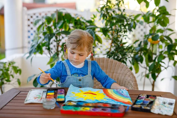 Pequena menina pintando arco-íris e sol com cores de água durante a pandemia coronavírus quarentena doença. Crianças pintando arco-íris ao redor do mundo com as palavras Lets all be well. Criança feliz — Fotografia de Stock