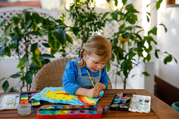 Küçük kız salgın koronavirüs hastalığı sırasında gökkuşağı ve güneşi sulu renklerle boyuyor. Dünyanın dört bir yanında çocuklar gökkuşağı resmi yapıyor. "Hepimiz iyi olalım". Mutlu çocuk — Stok fotoğraf