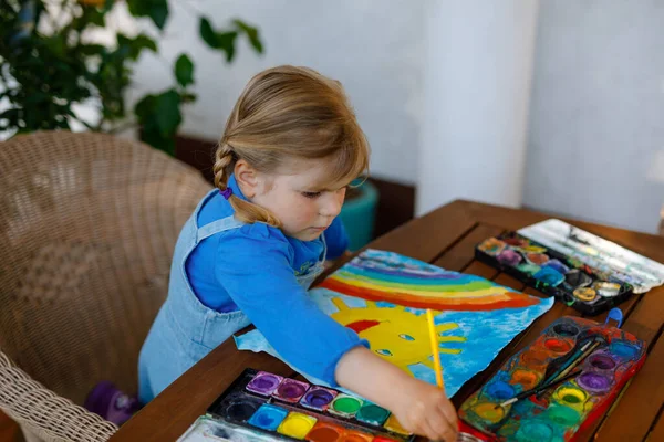 Kleine peuter meisje schilderen regenboog en zon met aquarantine ziekte tijdens pandemische coronavirus. Kinderen schilderen regenbogen over de hele wereld met de woorden Laten we allemaal goed zijn. Gelukkig kind — Stockfoto