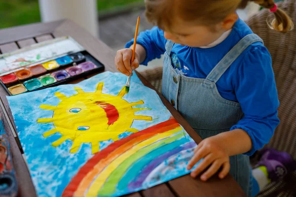 Kleine peuter meisje schilderen regenboog en zon met aquarantine ziekte tijdens pandemische coronavirus. Kinderen schilderen regenbogen over de hele wereld met de woorden Laten we allemaal goed zijn. Gelukkig kind — Stockfoto