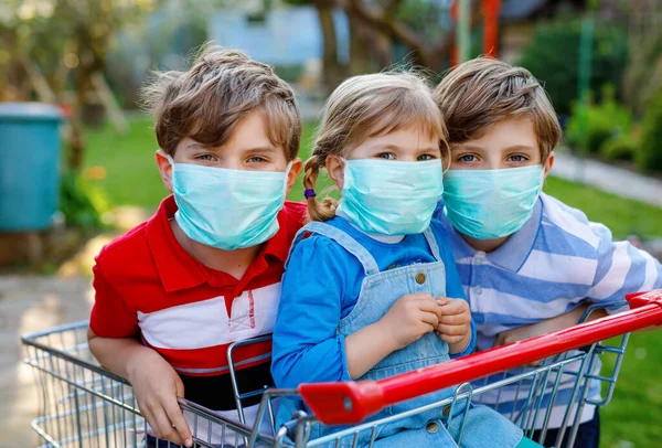Троє дітей, маленька дівчинка-малюк і двоє хлопчиків у медичній масці як захист від пандемії коронавірусної хвороби. Діти з кошиком використовують захисне обладнання як боротьбу з ковадлом 19 . — стокове фото