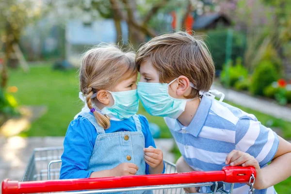 Dos niños, la niña y el niño de la escuela en máscara médica como protección contra la enfermedad pandémica por coronavirus. Niños hermanos con carrito de la compra utilizando equipo de protección como lucha con covid 19. — Foto de Stock