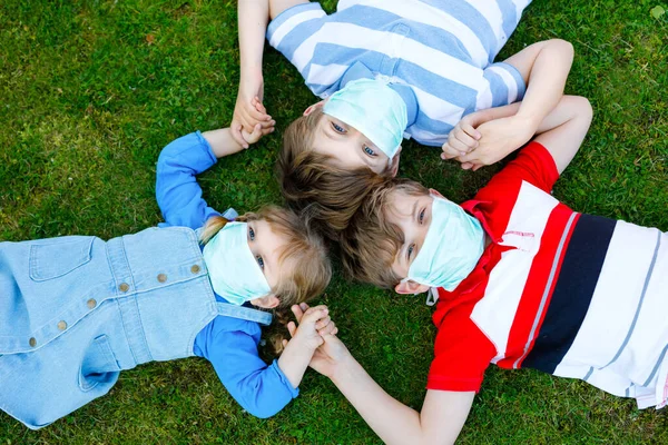Três crianças, uma criança e dois miúdos mascarados como protecção contra a doença pandémica do coronavírus. Crianças, irmãos adoráveis usando equipamentos de proteção como luta contra o covid 19. — Fotografia de Stock