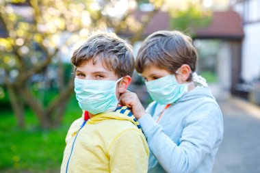 Salgın koronavirüs hastalığına karşı korunmak için maske takan iki çocuk. Çocuklar, sevimli kardeşler ve en iyi arkadaşlar koruma ekipmanlarını kovid 19 'a karşı savaşmak için kullanıyorlar..