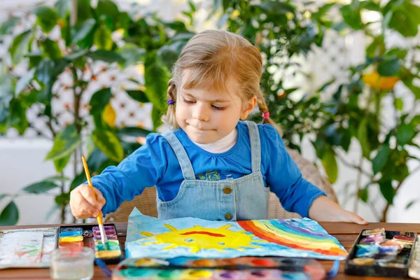 Маленькая девочка рисовала радугу и солнце акварелью во время пандемического коронавирусного карантина. Дети рисуют радуги по всему миру со словами "Давайте все будем здоровы". Счастливый ребенок — стоковое фото