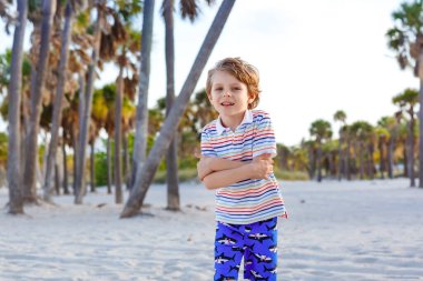 Miami sahilinde eğlenen sevimli, aktif bir çocuk, Key Biscayne. Mutlu şirin çocuk rahatlıyor, kumla oynuyor ve palmiyelerin ve okyanusun yanında güneşli bir günün tadını çıkarıyor.