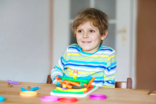 Gülümseyen anaokulu çocuğu hamurla eğleniyor, renkli modelleme bileşik kiliyle. Çocuklarla yaratıcı bir eğlence. Corona virüsü karantinası sırasında evde kalmak. Sığınma yeri, tecrit kavramı, — Stok fotoğraf