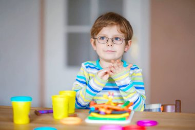 Gülümseyen anaokulu çocuğu hamurla eğleniyor, renkli modelleme bileşik kiliyle. Çocuklarla yaratıcı bir eğlence. Corona virüsü karantinası sırasında evde kalmak. Sığınma yeri, tecrit kavramı,