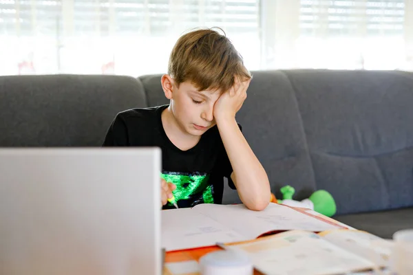 Upset school kid boy making homework during quarantine time from corona pandemic disease. Frustrated sad boy learning staying at home with video via laptop. Homeschooling concept — Stock Photo, Image