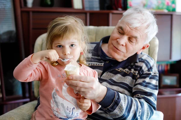 Happy grandfather and cute little toddler granddaughter, adorable child eating together ice cream. Family tasting sweet icecream, baby girl feeding senior man. — Stock Photo, Image