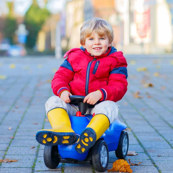 Felice ragazzo carino in vestiti colorati moda guida auto giocattolo. bambino si diverte, all'aperto. Tempo libero per bambini attivo in autunno . — Foto Stock