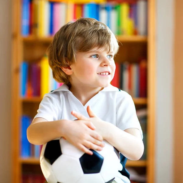 Pequeño niño rubio preescolar con pelota viendo el partido de fútbol en la televisión. Divertido niño feliz llorando ventilador divertirse y animar equipo de fútbol ganador. Campeones y concepto de copa del mundo — Foto de Stock