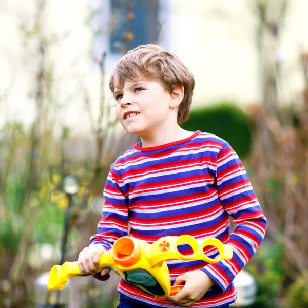 Chlapeček si hraje s vodní pistolí na jarní zahradě. Školák se baví a hraje. Vtipné dítě těší teplé sezóny a hry venku — Stock fotografie