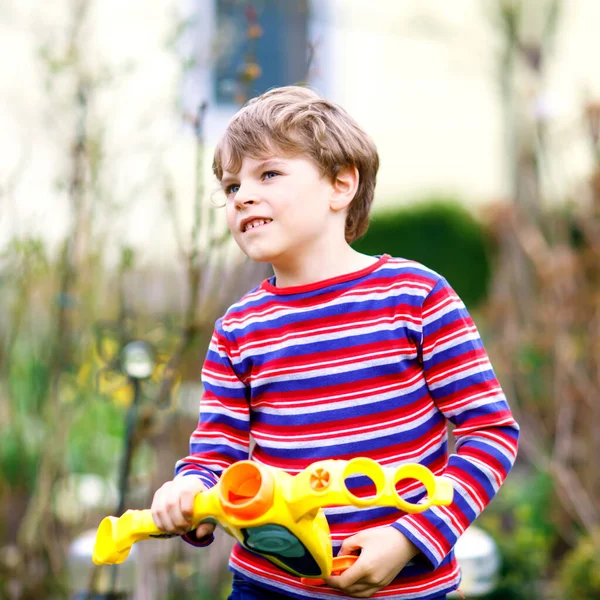 Un ragazzino che gioca con la pistola ad acqua nel giardino primaverile. Studentessa che si diverte e agisce. Bambino divertente godersi la stagione calda e giochi all'aperto — Foto Stock