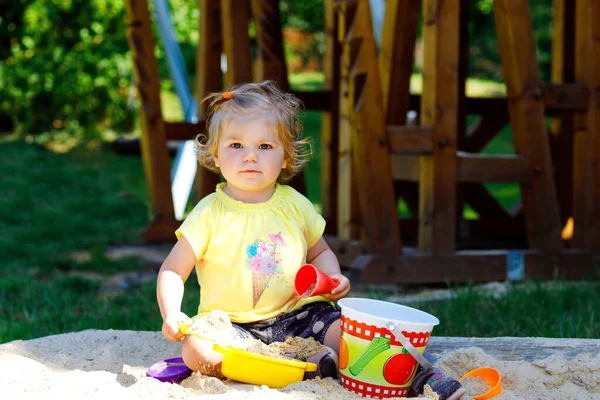 Roztomilé batole dívka hraje v písku na venkovním hřišti. Krásné dítě baví na slunné teplé léto slunečný den. Šťastné zdravé dítě s pískem hračky a v barevné módní oblečení. — Stock fotografie