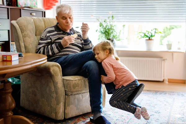 Happy grandfather and cute little toddler granddaughter, adorable child playing together at home, indoors. Family, baby and senior man having fun — Stock Photo, Image