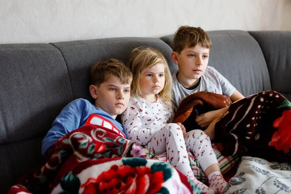 Bella bambina e due ragazzini che guardano cartoni animati o film in TV. Tre bambini sani e felici, fratelli durante la quarantena del coronavirus che rimangono a casa. Fratelli e sorelle insieme. — Foto Stock