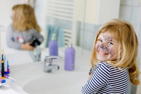 Menina pequena engraçada usando mães compõem e pintam o rosto com sombras de olhos. Criança de bebê feliz que faz experimentos com cosméticos da mãe. Miúdo à volta — Fotografia de Stock