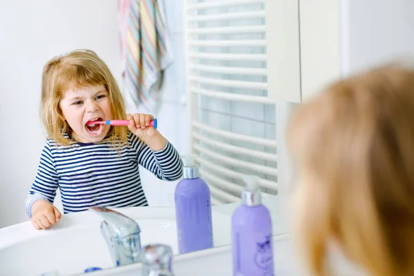 Schattig klein meisje met een tandenborstel in haar hand reinigt haar tanden en glimlacht. Grappig gelukkig gezond kind leren ochtend routing met wassen gezicht en het reinigen van tanden — Stockfoto