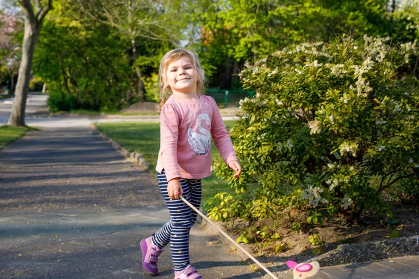 Pequena menina criança andando no parque no dia ensolarado da primavera. Bonito adorável criança brincando com empurrando animal de brinquedo de madeira sobre rodas — Fotografia de Stock
