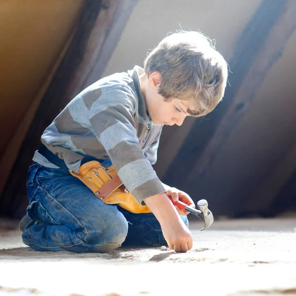 Kleiner Junge hilft mit Spielzeug auf Baustelle. Lustiges Kind von 6 Jahren, das Spaß am Bau eines neuen Familienhauses hat. Kind mit Nägeln und Hammer hilft Vater bei Renovierung von altem Haus. — Stockfoto