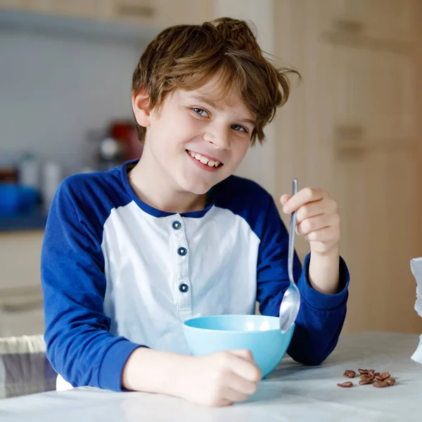 Счастливый маленький блондин, который ест хлопья на завтрак или обед. Здоровое питание для детей. Ребенок в красочной пижаме завтракает с молоком и мюсли . — стоковое фото