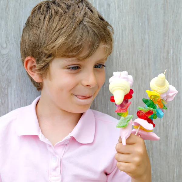 Gelukkige kleine jongen met marshmallow spies in de hand. Kind met verschillende onhelse kleurrijke snoepjes — Stockfoto