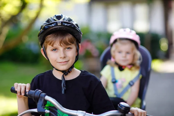 Ritratto di bambina con casco di sicurezza seduta sul seggiolino del fratello. Ragazzo in bicicletta con una sorella adorabile. Concetto di sicurezza e protezione dei minori. Viaggio attività week-end in famiglia . — Foto Stock