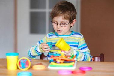 Gülümseyen anaokulu çocuğu hamurla eğleniyor, renkli modelleme bileşik kiliyle. Çocuklarla yaratıcı bir eğlence. Corona virüsü karantinası sırasında evde kalmak. Sığınma yeri, tecrit kavramı,