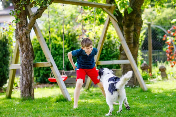 Actieve jongen spelen met familie hond in de tuin. Lachend schoolkind dat plezier heeft met de hond, met rennen en spelen met de bal. Gelukkige familie buiten. Vriendschap tussen dier en kind — Stockfoto