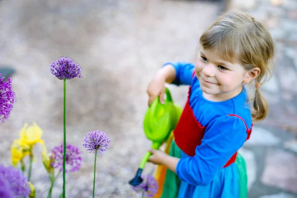 Bella bambina in stivali di gomma gialla e colorato vestito irrigazione fiori primaverili con acqua per bambini può. Bambino felice che aiuta nel giardino di famiglia, all'aperto. — Foto Stock