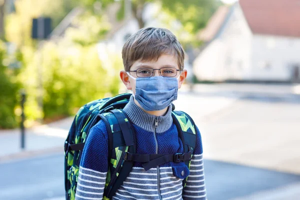 Happy little kid boy with glasses, medical mask and backpack or satchel. Schoolkid on way to school. Healthy adorable child outdoors. Back to school after quarantine time from corona pandemic disease — Stock Photo, Image