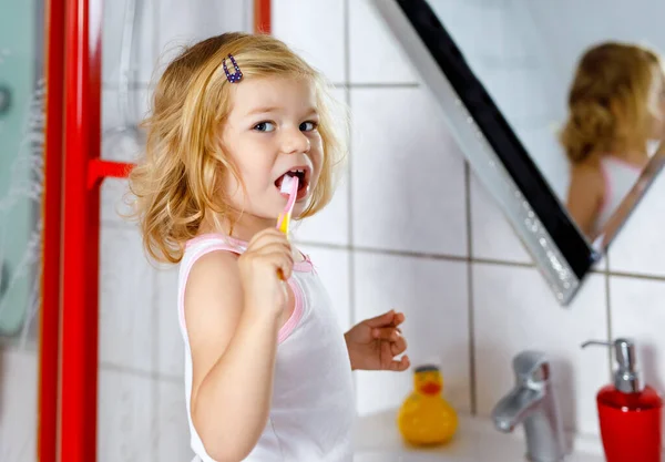 Menina adorável bonito criança segurando escova de dentes e escovar os primeiros dentes no banheiro depois de dormir. Linda criança bebê aprendendo a limpar o dente de leite. Manhã rotina de higiene saudável para crianças — Fotografia de Stock