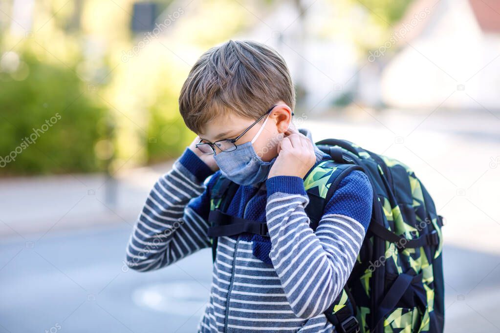 Happy little kid boy with glasses, medical mask and backpack or satchel. Schoolkid on way to school. Healthy adorable child outdoors. Back to school after quarantine time from corona pandemic disease