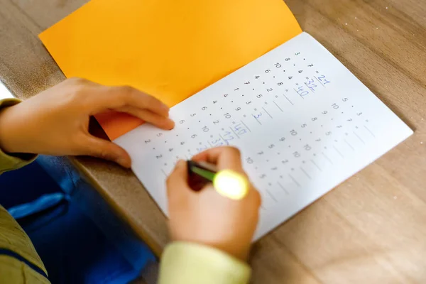 Niño de la escuela haciendo la tarea de matemáticas durante la cuarentena de la enfermedad pandémica corona. niño practica tablas de multiplicación y matemáticas básicas escribiendo con bolígrafo, quedándose en casa. Concepto de educación en el hogar —  Fotos de Stock