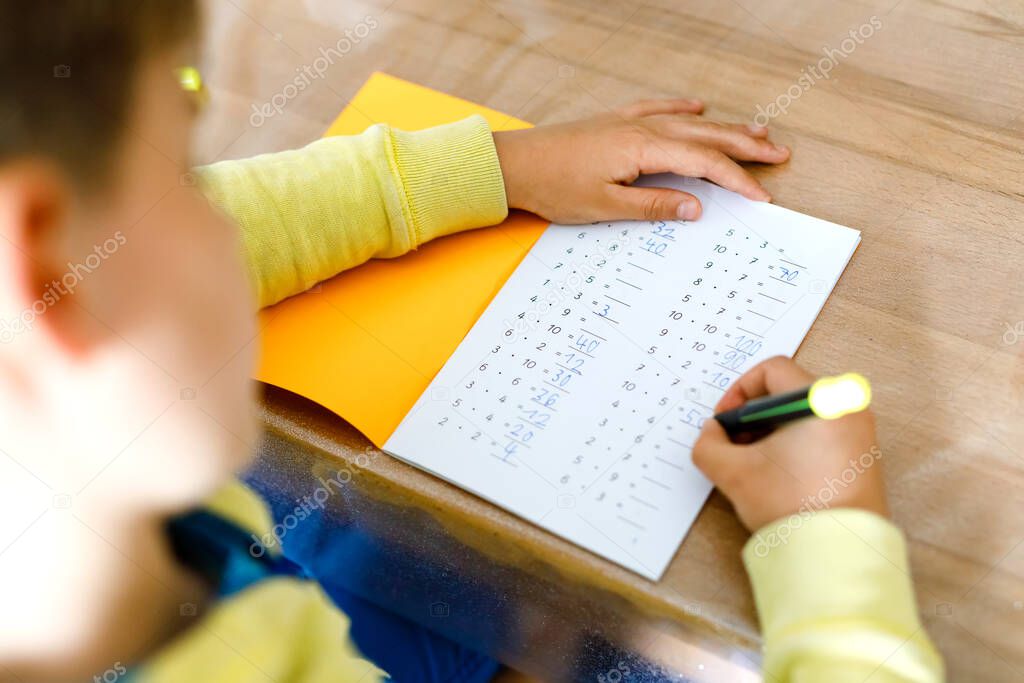 school kid making mathematics homework during quarantine from corona pandemic disease. child practice multiplication tables and maths basics writing with pen, staying at home. Homeschooling concept