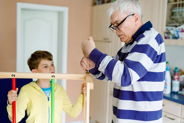 Little kid boy and grandfather working and constructing and repairing together. Senior man works with screwdriver and cute grandson learning. Happy family having fun together, granddad and child — Stock Photo, Image