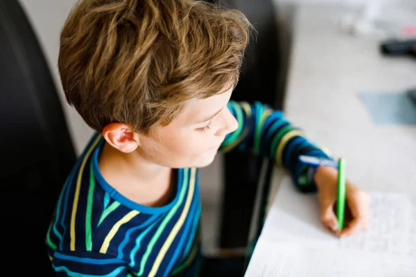 Un ragazzo della scuola felice che lavora sodo facendo i compiti durante la quarantena per una pandemia coronarica. Bambino sano che scrive con la penna, rimanendo a casa. Concetto di istruzione a casa — Foto Stock