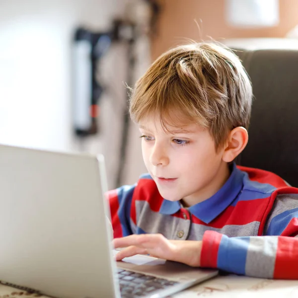 En liten skolunge som gör läxor på datorn. Barn lär sig på datorn. Hårt arbetande pojke gör motion under karantänstid från koronapandemisk sjukdom. Hemskolekoncept. — Stockfoto