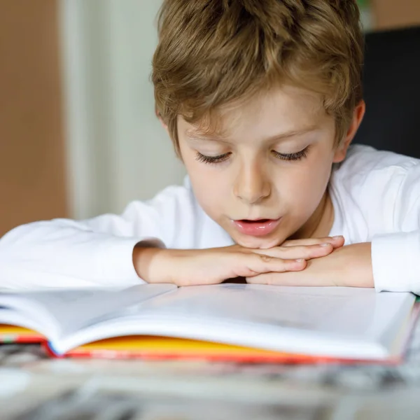 En blond skolpojke som läser en bok hemma. Barn intresserade av att läsa tidningen för barn. Fritid för barn, bygga färdigheter och utbildning koncept — Stockfoto