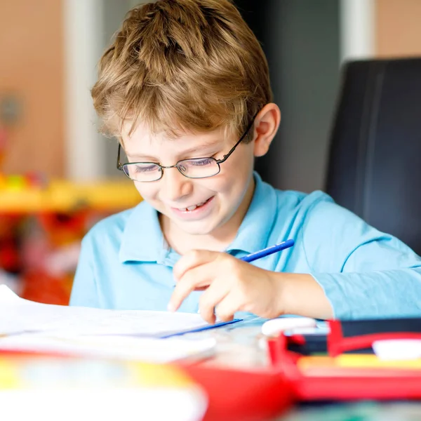 Милый маленький мальчик в очках дома, делает домашнее задание, пишет письма и делает математику цветными ручками. Маленький ребенок занимается спортом в помещении. Начальная школа и образование, представьте себе фантазию — стоковое фото