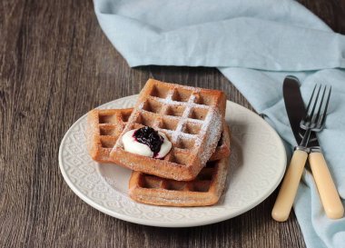 Pudra şekeri ve ahşap masa üzerinde krema ile geleneksel Belçika waffle. Gurme kahvaltı. 