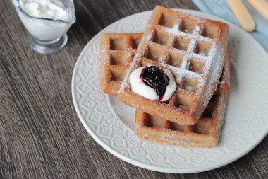 Pudra şekeri ve ahşap masa üzerinde krema ile geleneksel Belçika waffle. Gurme kahvaltı. 