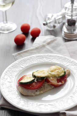 Fırında pişmiş domates, kabak ve peynir bir plaka üzerinde morina balığı fileto