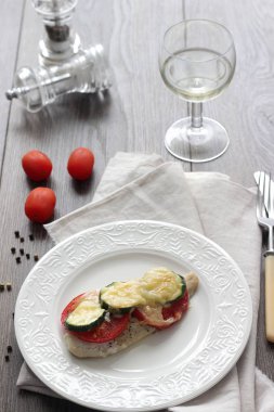 Fırında pişmiş domates, kabak ve peynir bir plaka üzerinde morina balığı fileto