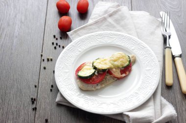 Fırında pişmiş domates, kabak ve peynir bir plaka üzerinde morina balığı fileto